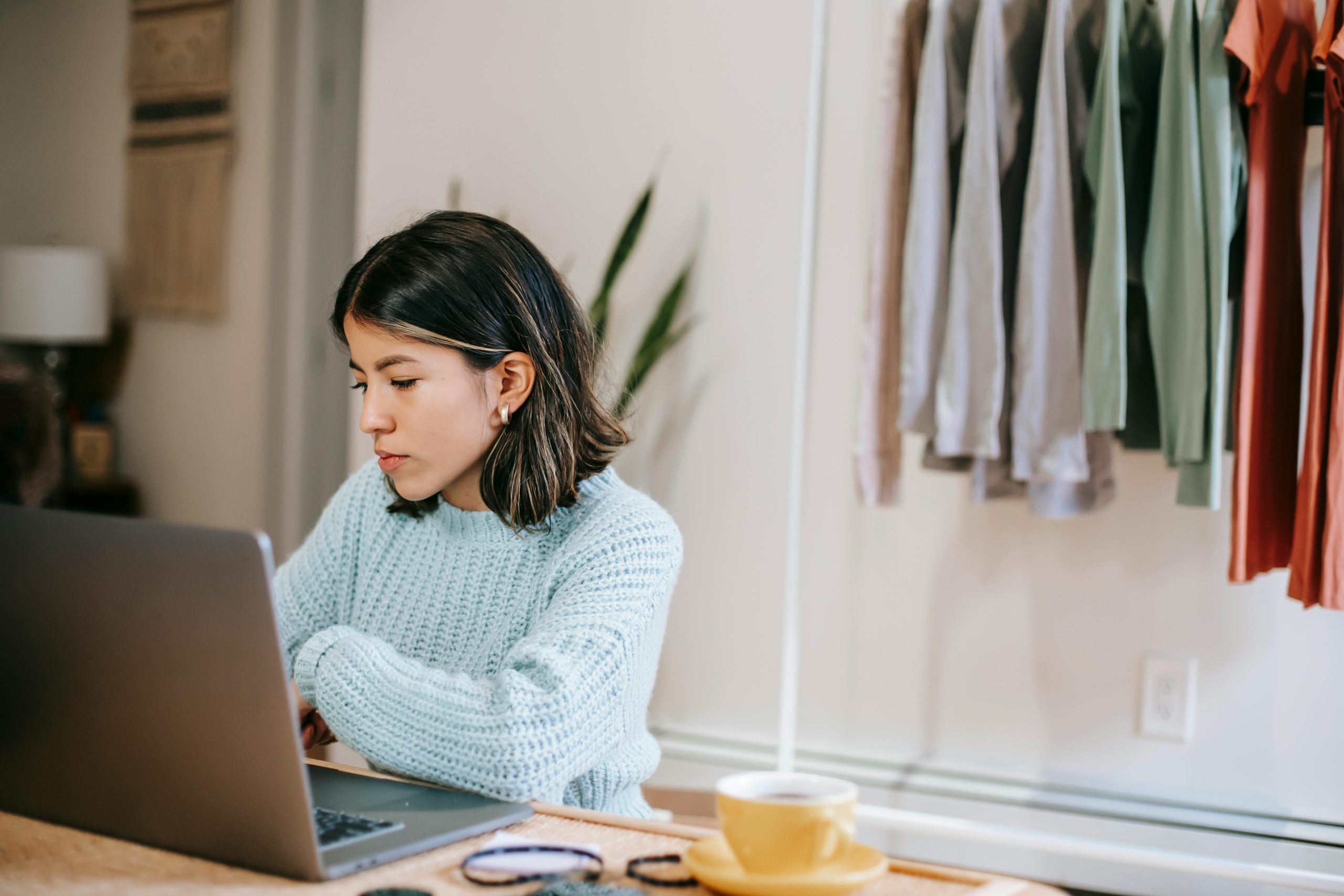 A professional woman is seen sitting at a computer with a hanging rack of clothes behind her