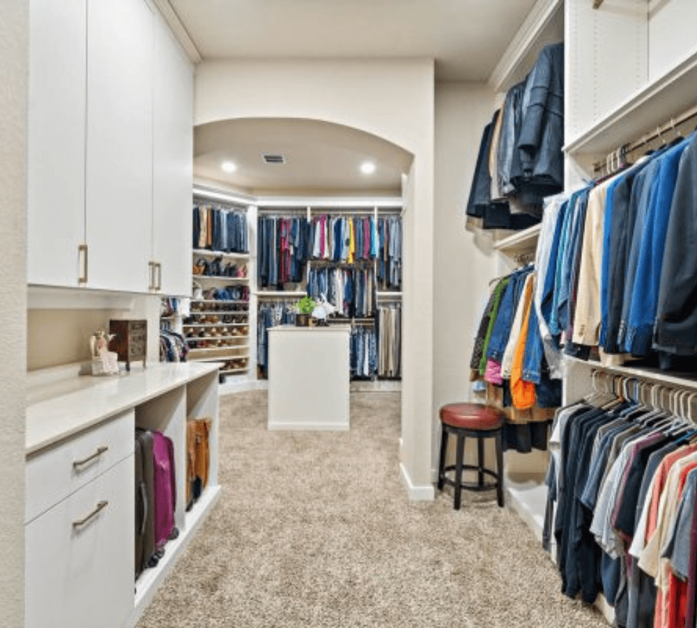Custom walk-in closet design with built-in shelving, hanging storage, center island, and carpeted flooring in Houston home