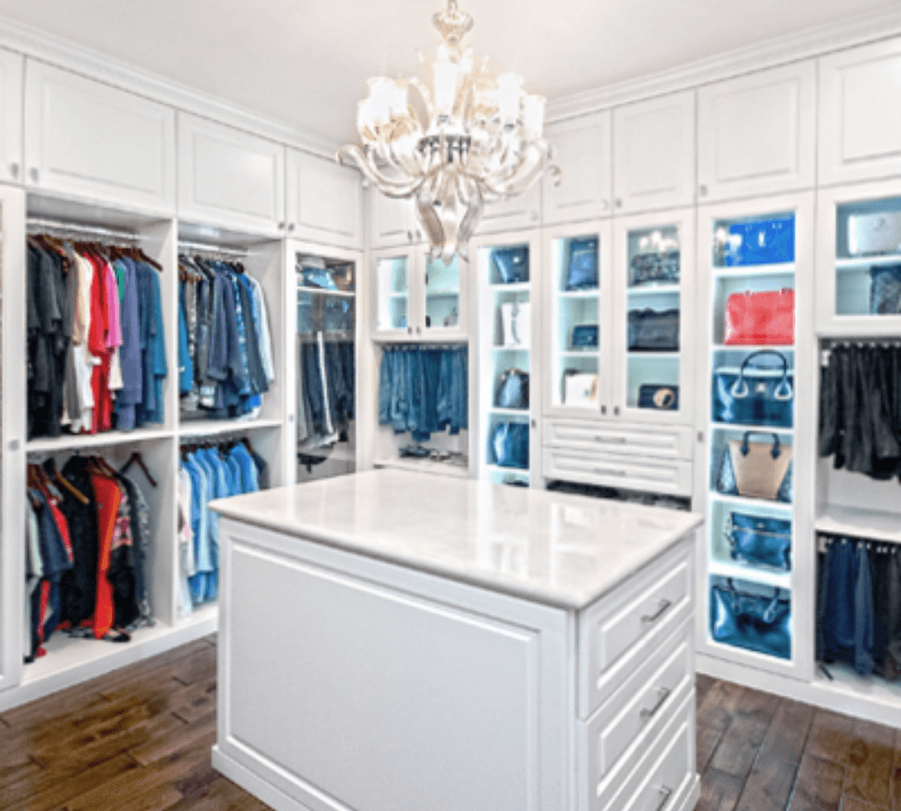 An all-white closet with a chandelier, middle island, cabinets, and shelving.