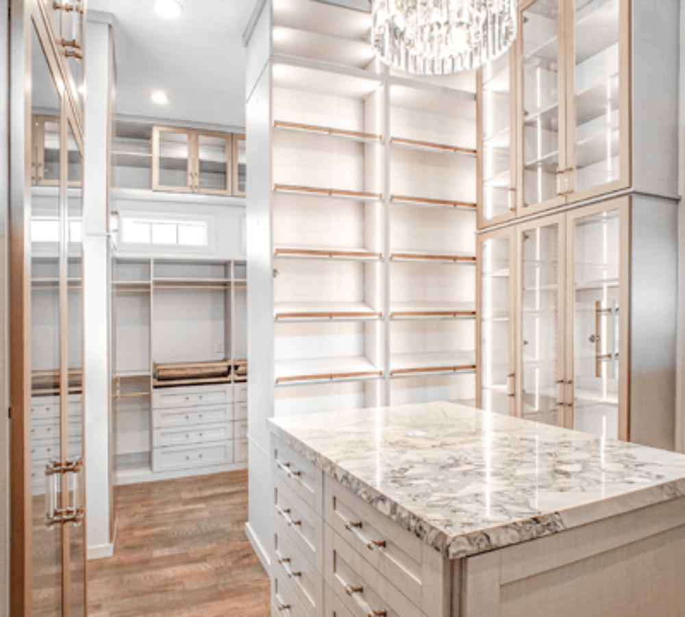 A tan and white closet with a chandelier, hanger space, shelving, and wood accents.