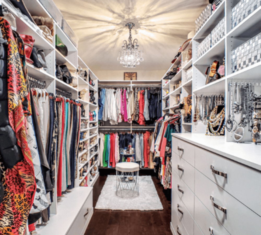 An all-white closet with hangers and drawers that is full of clothes and accessories.
